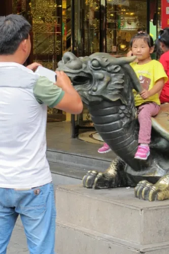 A man takes a photo of a small child sitting on a sculpture dragon in Shanghai's Yuyuan Bazaar. Photo by BF Newhall
