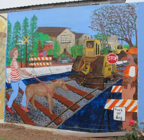 Jill-McLennan "Jingletown," a mural by Jill McLennan on the Rue de Merde, Jingletown, Oakland, CA. It shows a woman walking her dog. Photo by BF Newhall