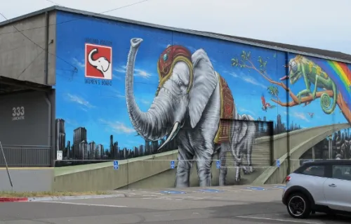 elephant-mural A mural embellishes the logo of the Oakland Museum Women's Board on Lancaster Street, Jingletown, Oakland, CA. The mural depicts an elephat with raised trunk. Photo by BF Newhall