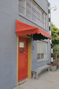 The entrance to the gray Berkeley Potters Guild building is a red door with red awning. Photo by BF Newhall