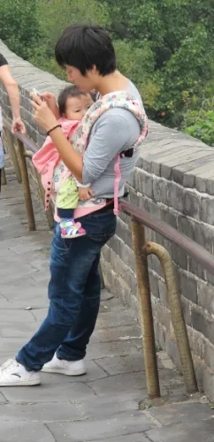 a man carrying a baby in a chest pack checks his cell phone on the Great Wall of China. PHoto by BF Newhall