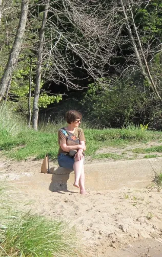 a woman sits on a cement dam alongside a channel emerging from a woods on lake michigan. photo by BF Newhlall