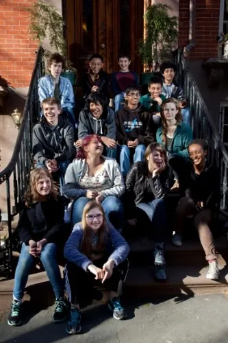 A dozen or so happy teenagers sit on the front steps of a brick building. The editorial board of KidSpirit meets to discuss future issues. Photo c 2014 by Jon Hochman