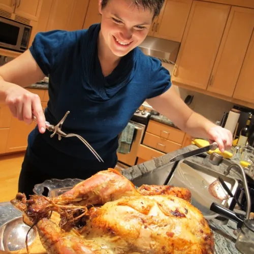 A young woman carves a browned roasted turkey in the kithcen. Photo by BF Newhall