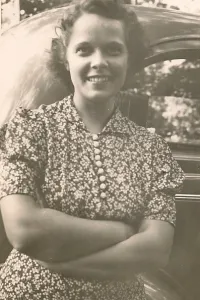 The mother of a temporarily lost child. A woman in flowered house dress with buttons leaning against a 1940s car. lost and found in downtown detroit in wartime. world war two. 