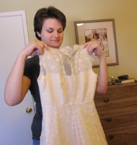Daughter holds up her mother's wedding dress and smiles. Photo by BF Newhall